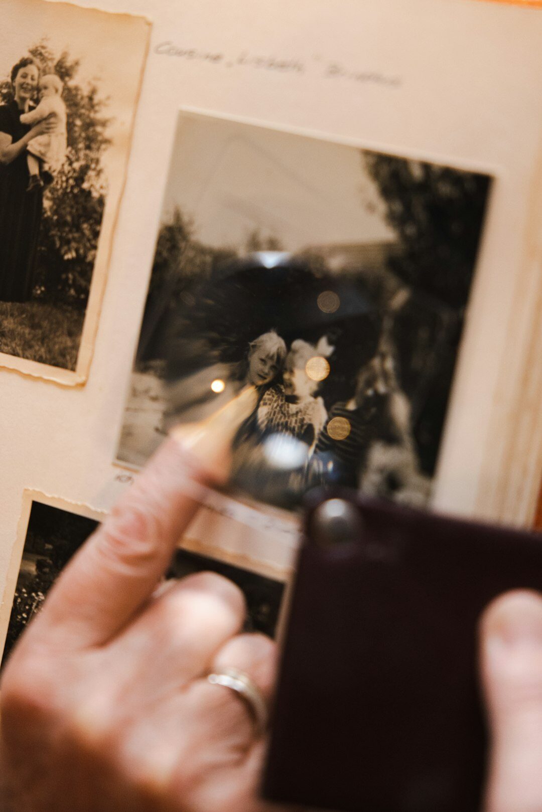 Hands holding a magnifying glass over old photographs